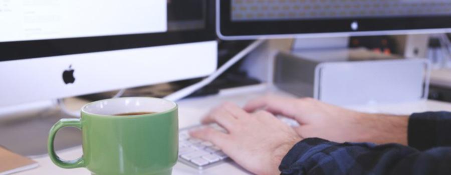 A man's hands typing on a keyboard with a green mug next to him.
