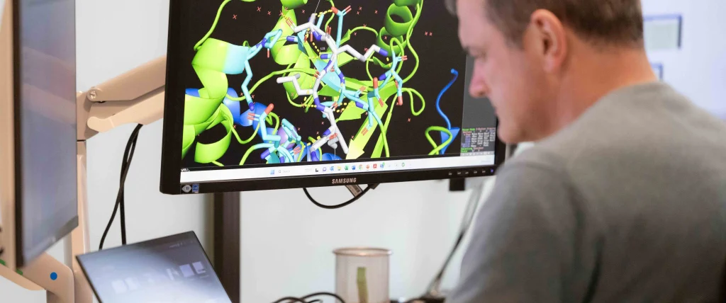 Man working in a lab at Apollo Therapeutics with a computer screen in the background