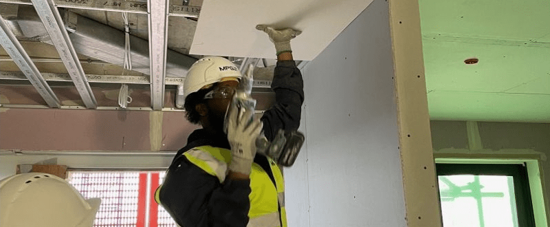 MPG Contracts worker with a drill fixing a piece of plasterboard to the ceiling of a building